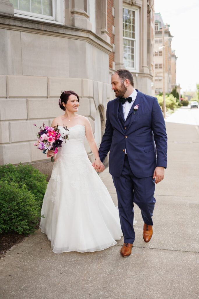 A smiling bride and groom. The bride holds a bouquet of vibrant pink flowers.