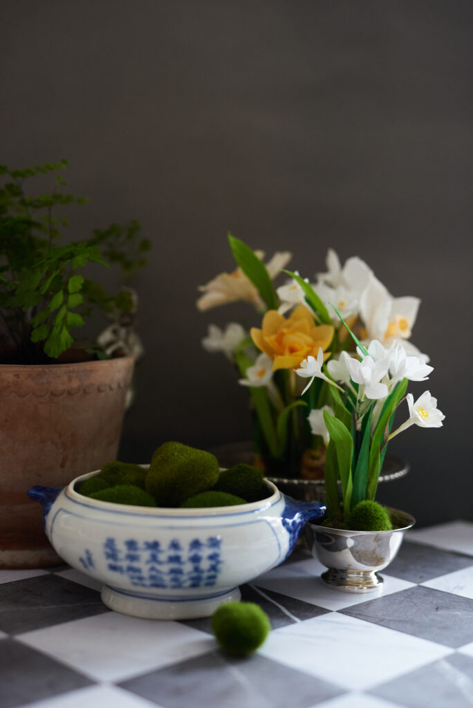 A still life arrangement of crepe paper daffodils and paper whites on a checkerboard floor