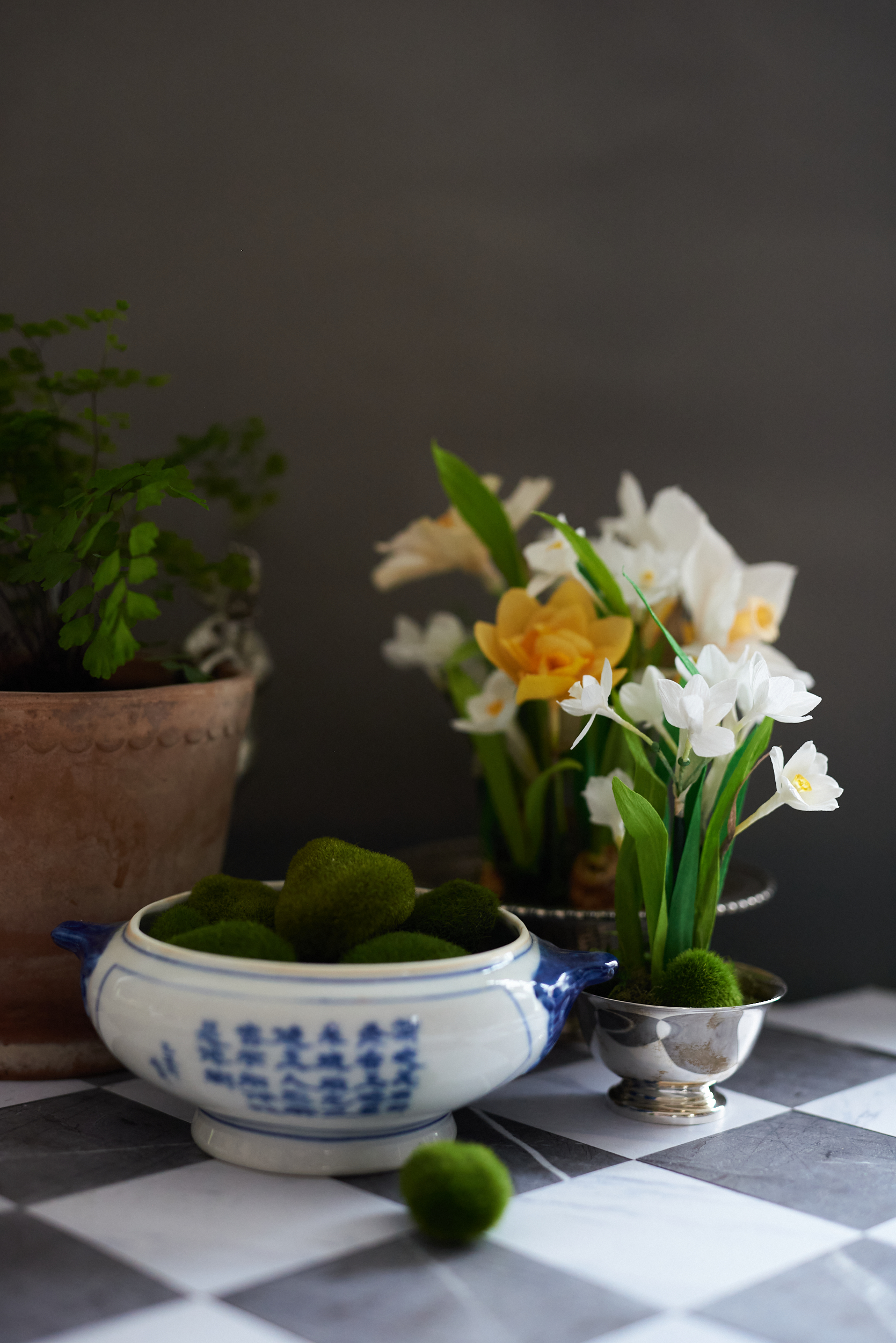 A still life arrangement of crepe paper daffodils and paper whites on a checkerboard floor